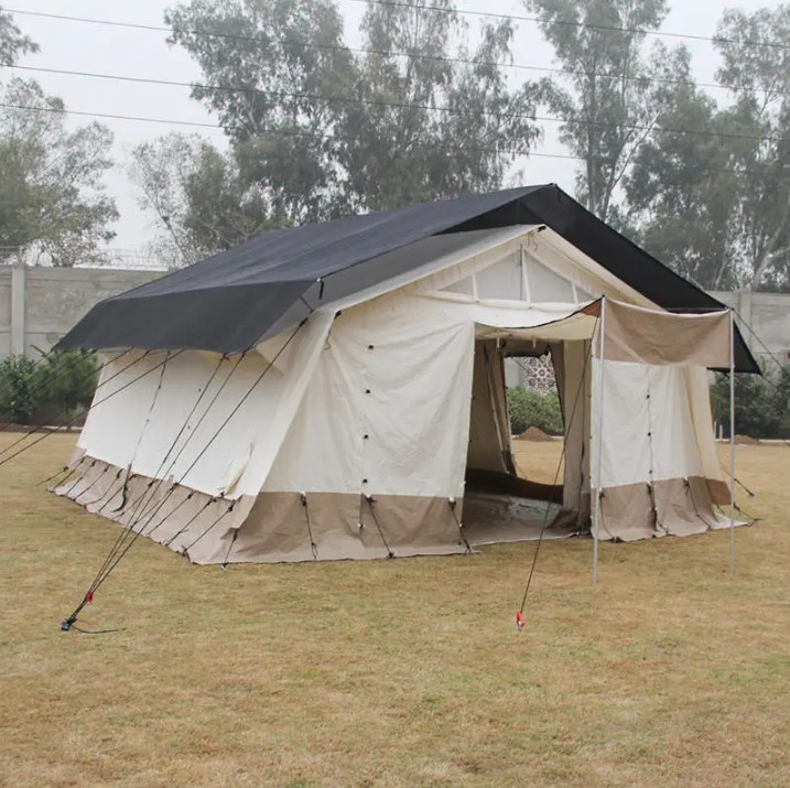 ICRC IFRC standard 33.6m2 multi-purpose shelter base tent deployed on grass showing full polyester-cotton structure with aluminium frame, dark roof fly sheet, cream walls, and mud flap skirt